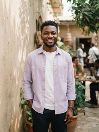 A smiling man in a lavender shirt standing in a sunlit courtyard